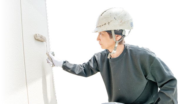 ローラーで白い塗料を外壁に塗っている職人